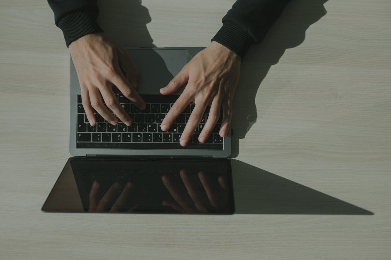 Overhead shot of hands typing on a laptop, showcasing technology and internet usage.